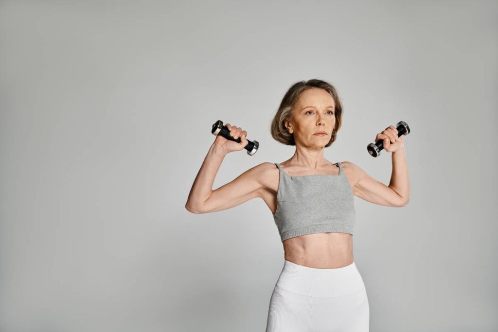 Attractive woman in active pose with dumbbells on gray background.